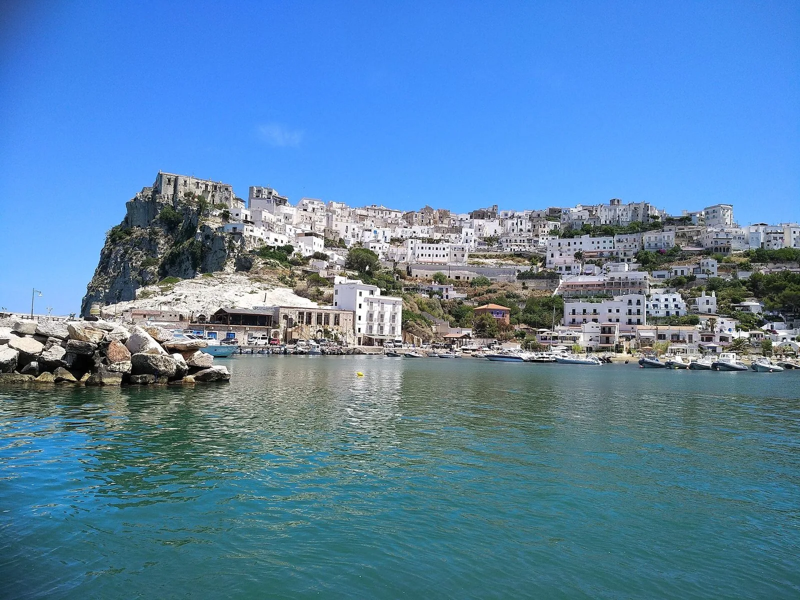 Peschici vista dal mare: le case bianche sullo sperone di roccia, il castello in cima alla scogliera e le barche ormeggiate nel porticciolo