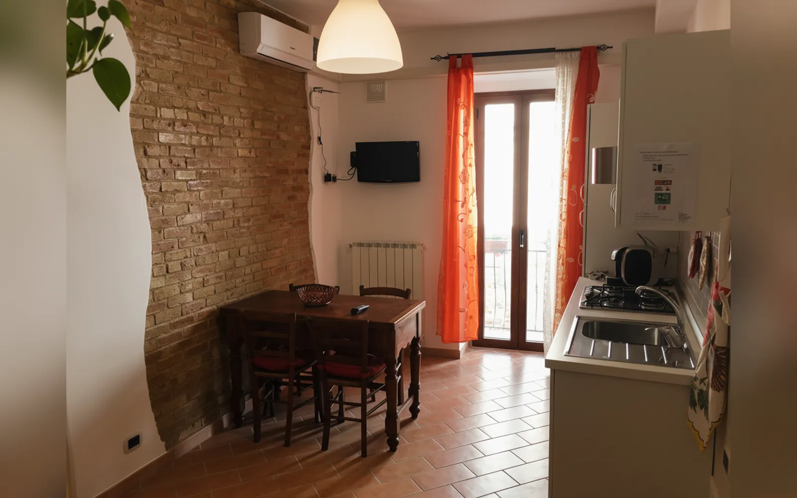 La cucina con il tavolo in legno, la parete in mattoni e la portafinestra