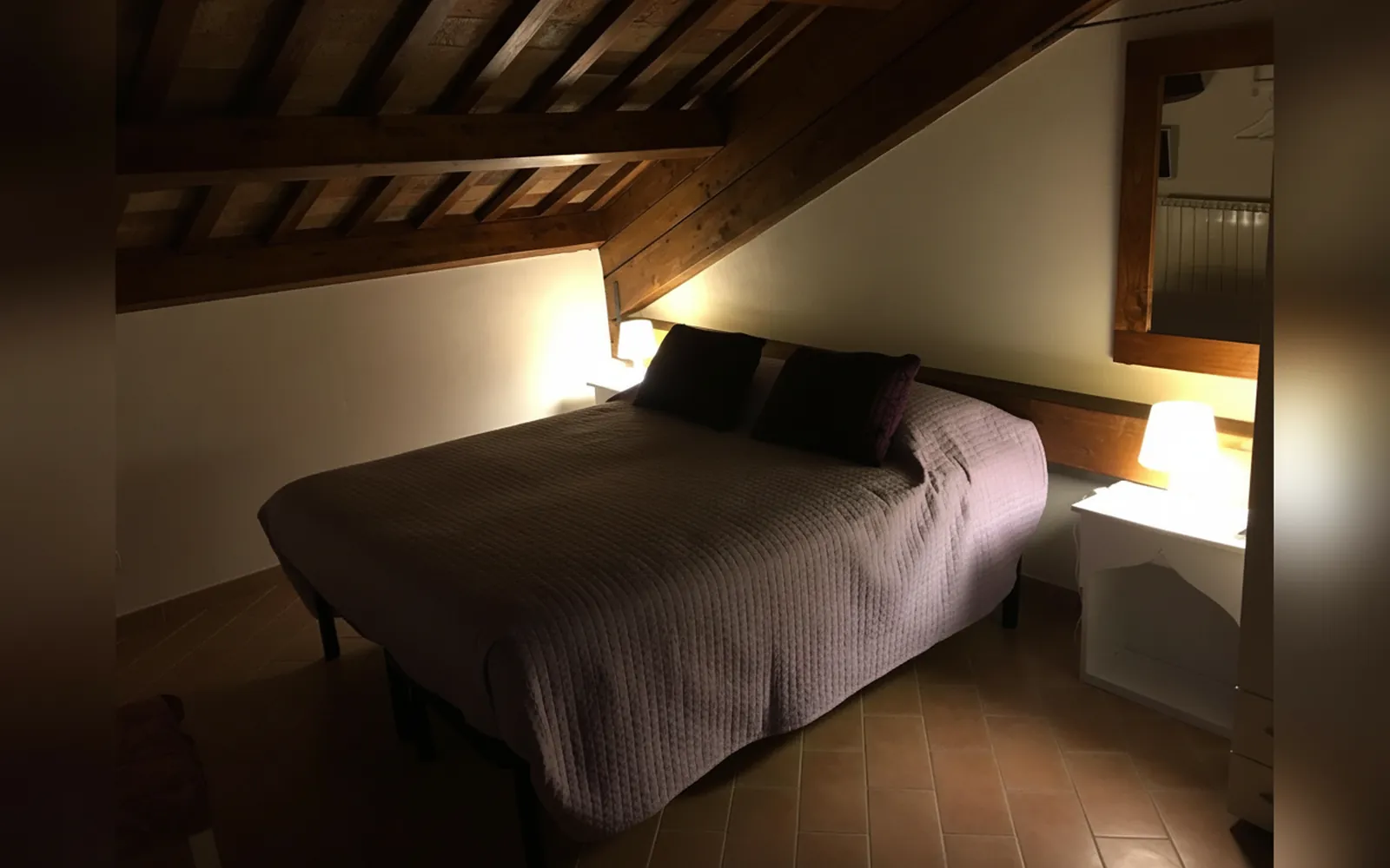 Il letto matrimoniale con i cuscini viola, sotto le travi del sottotetto